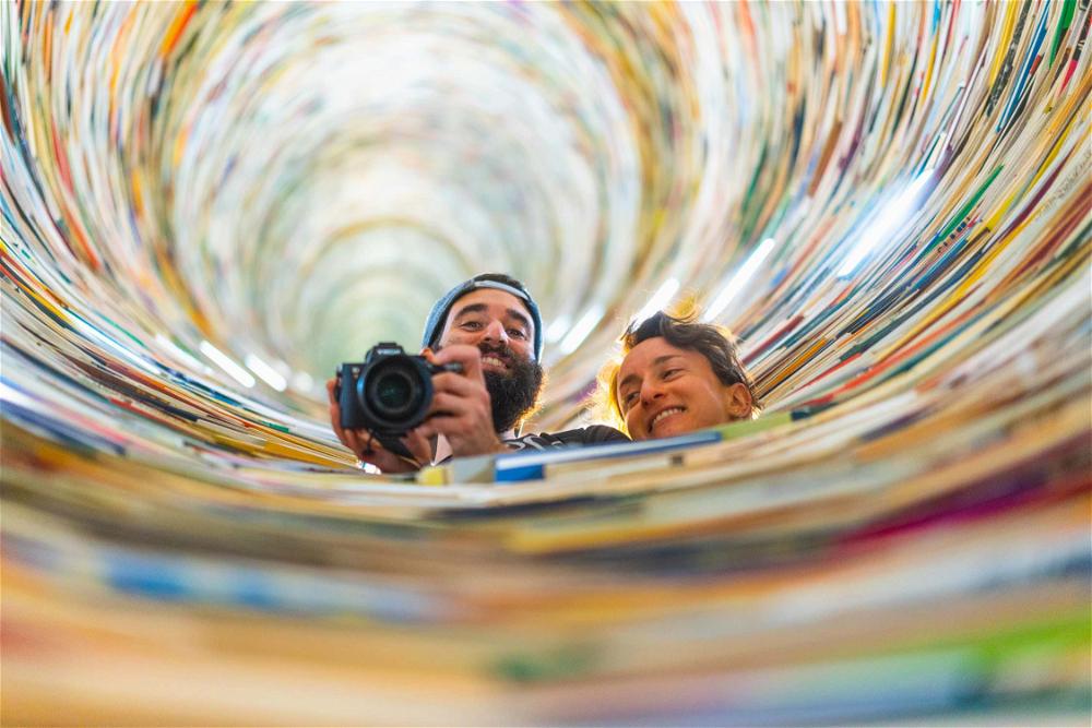 A man and woman taking a picture in a spiral of books.