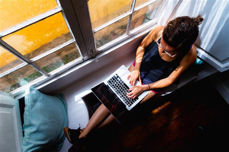 A woman using a laptop in front of a window.