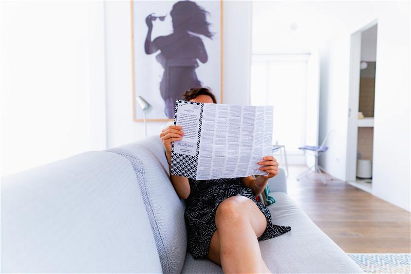 A woman sitting on a couch reading a newspaper.