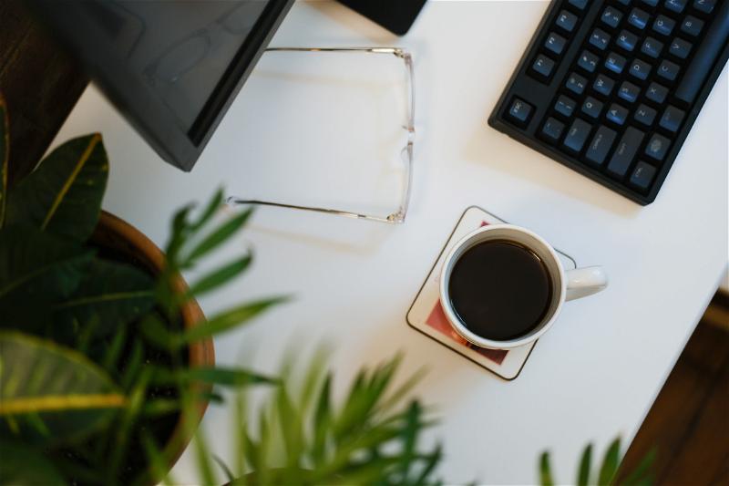 A cup of coffee on a desk next to a keyboard and plant.