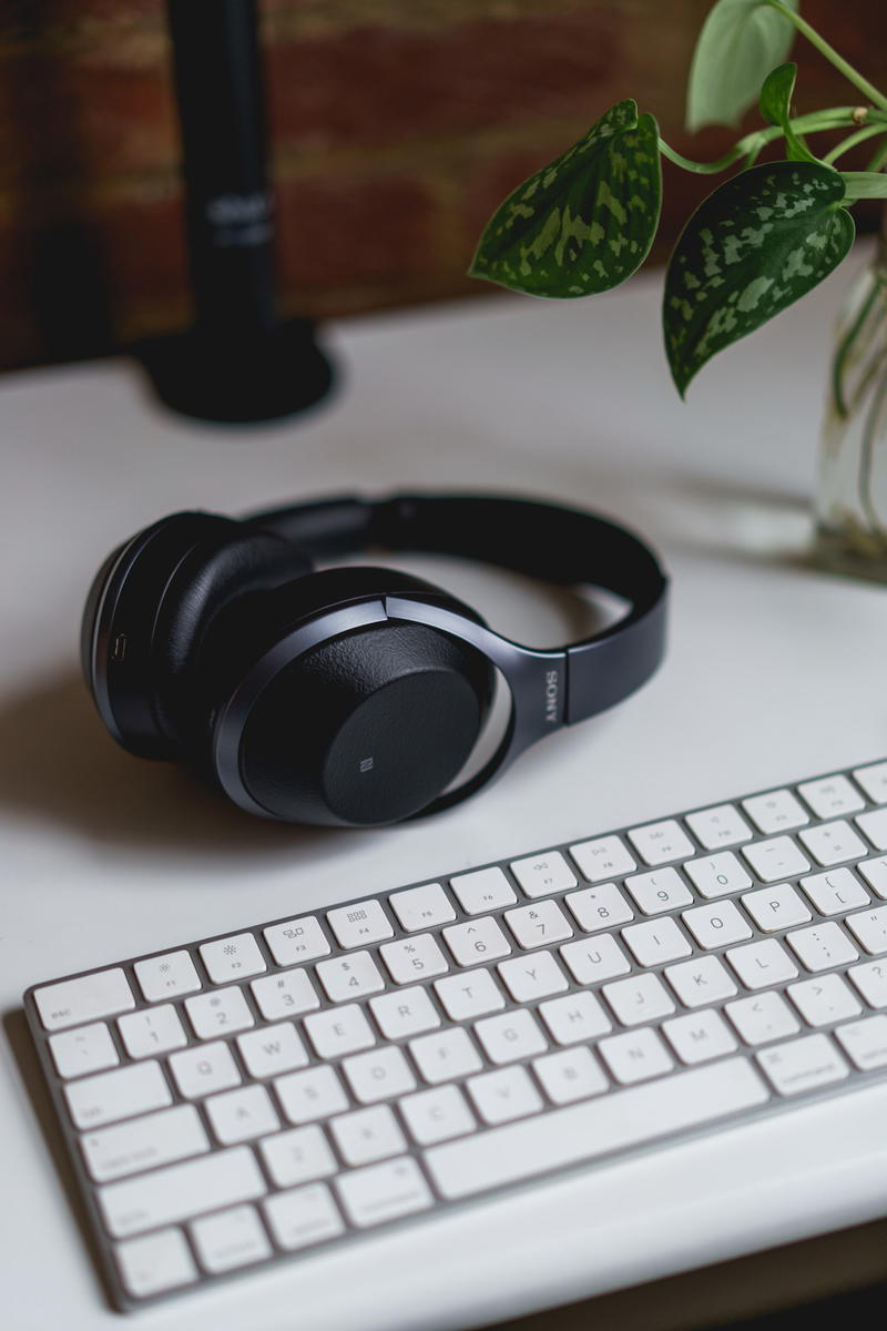 Sony noise canceling bluetooth headphones set next to the apple magic keyboard on a white home office desk