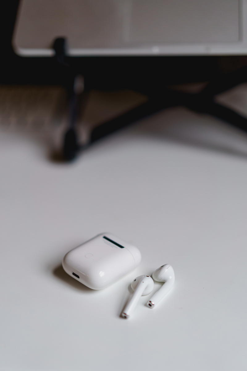 Airpods on a white table next to a laptop.