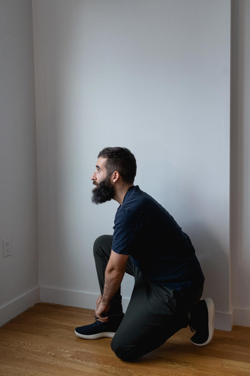 A man crouching on the floor in an empty room.