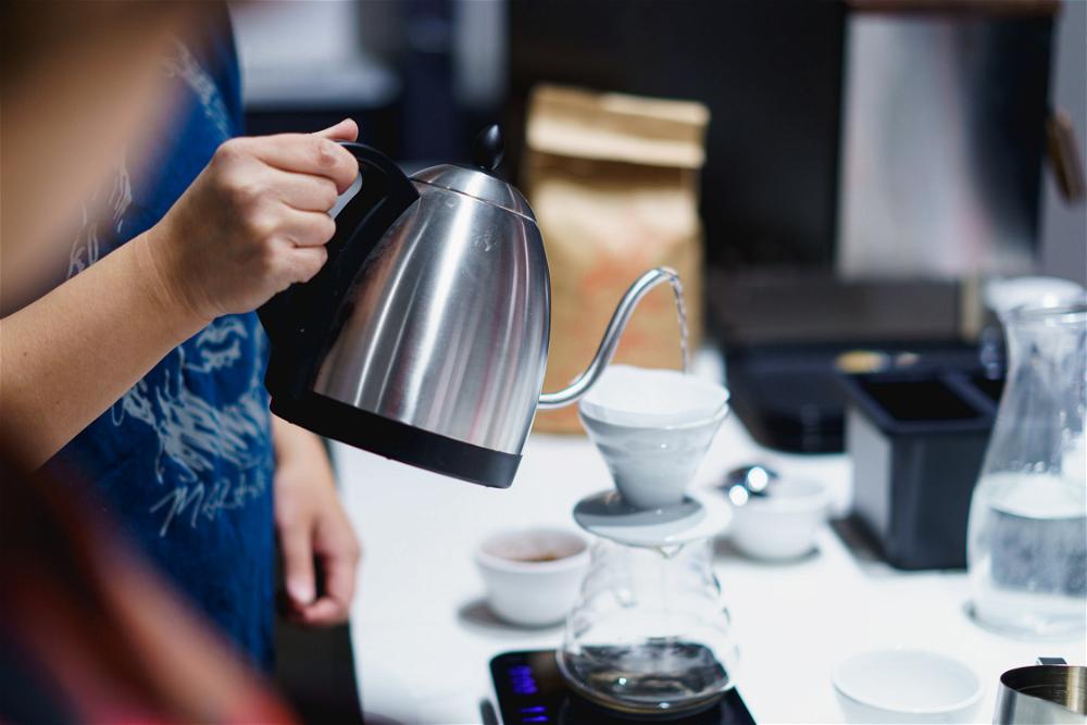 A woman pouring coffee into a kettle.