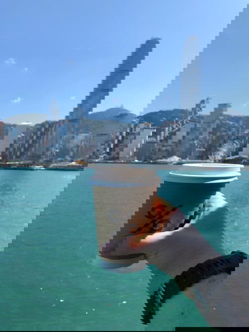 A person holding a coffee cup in front of a city.