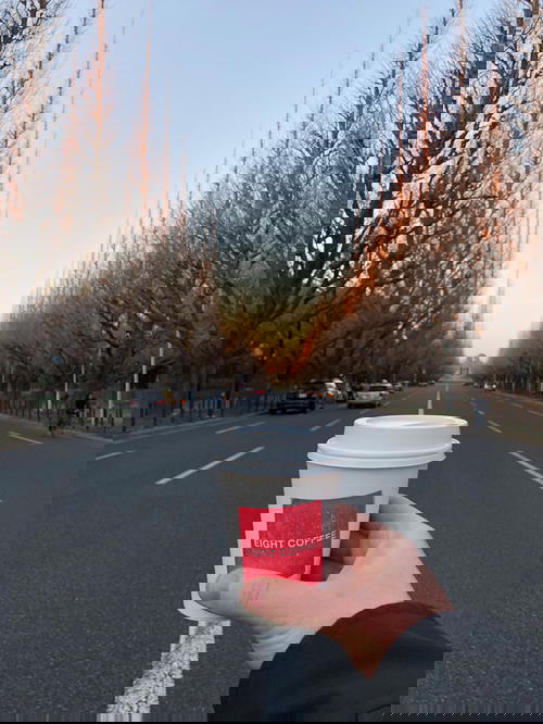 A person holding up a coffee cup in the middle of a street.