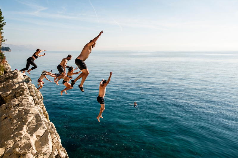 a group of people jumping off a cliff into the ocean