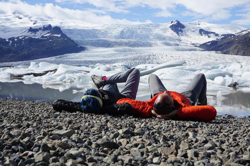 Two people laying on rocks with a glacier in the background.