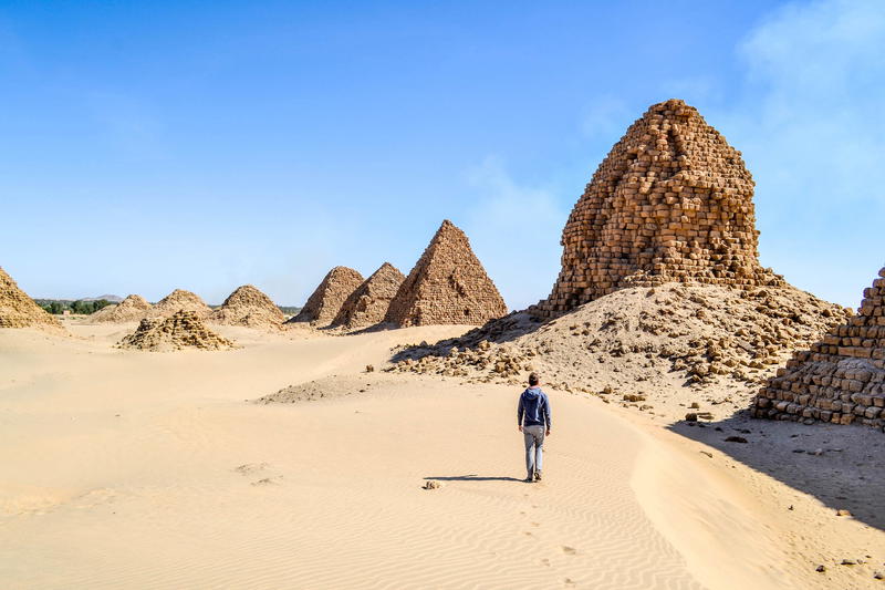 A man walking through the sand with pyramids in the background.