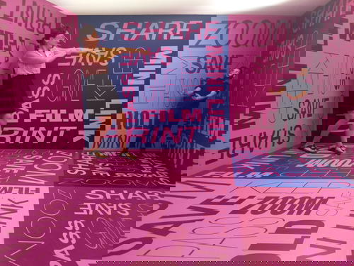 Two people standing in a pink room with words written on it.