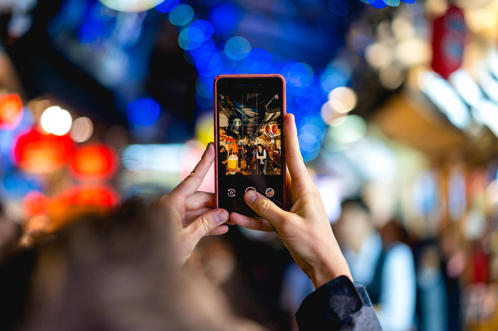 A person taking a picture with their phone in a busy street.