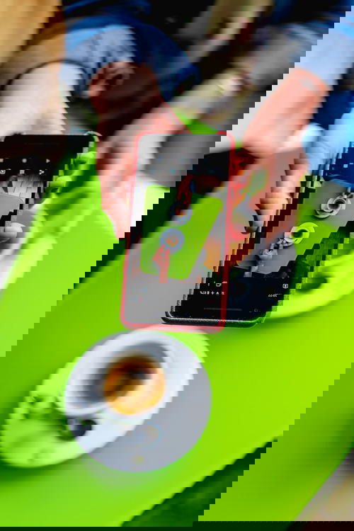 Woman holding Google Pixel phone to take a photo of two cups of coffee on a bright green table