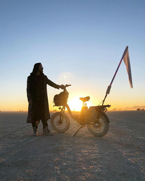 A man standing next to a bike with a flag on it.