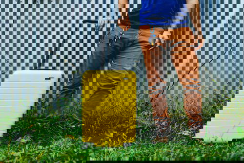 Man against a metal siding next to a yellow suitcase
