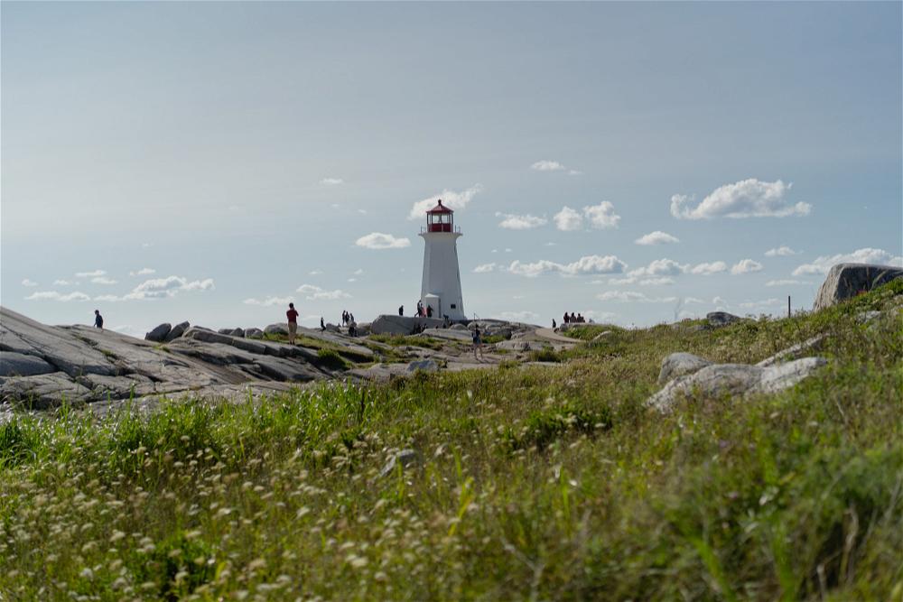 A lighthouse sits on top of a grassy hill.