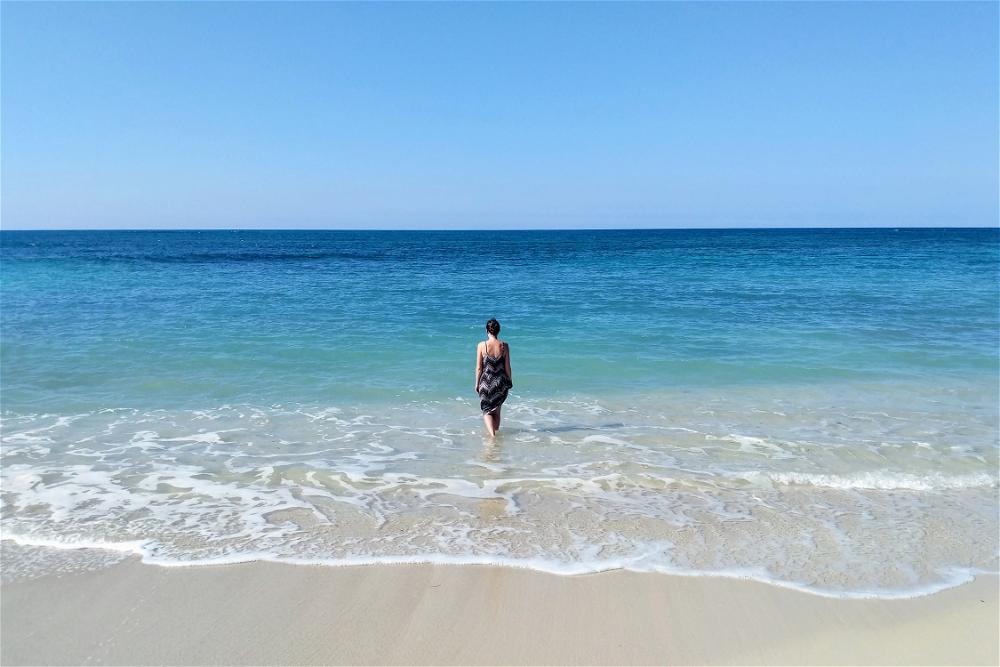 A woman standing on a beach looking at the ocean.