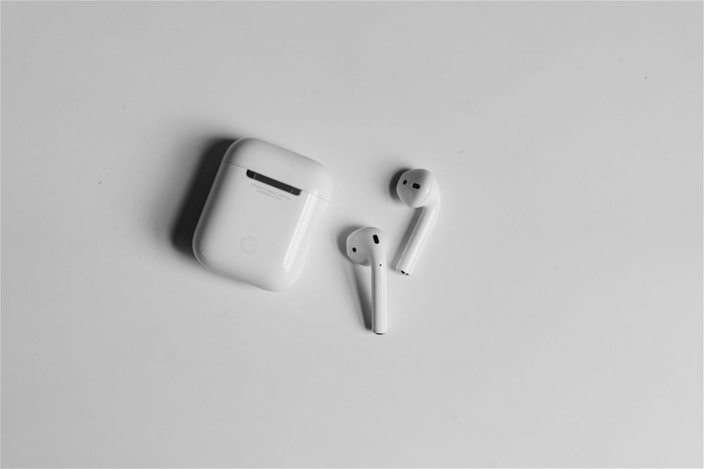 Apple Airpods case and 2 AirPod buds on a white table with shadows