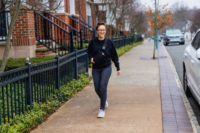 a woman walking down a sidewalk next to a car