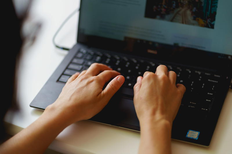 Woman typing on a black 13 inch laptop on a small white desk in a home office setup