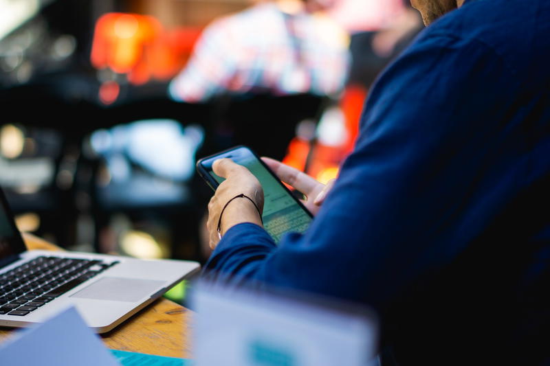 A person using a cell phone and laptop at a table.