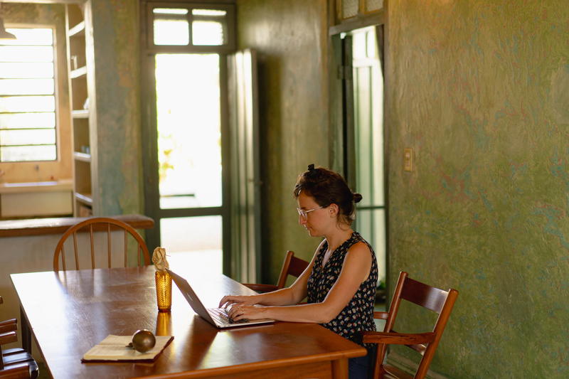 A woman sitting at a wooden table with a laptop.