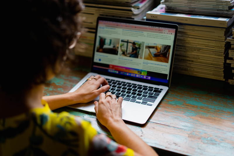 A woman typing on a laptop in front of a pile of books.