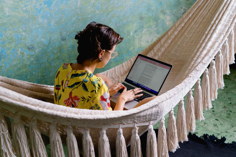 A woman using a laptop in a hammock.