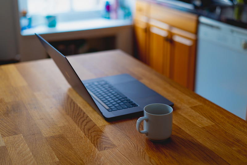 Coffee cup next to 16 inch MacBook setup on a wooden table working from home
