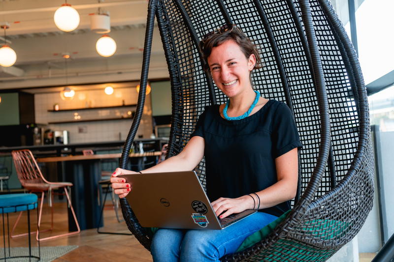 A woman sitting in a wicker chair with a laptop.