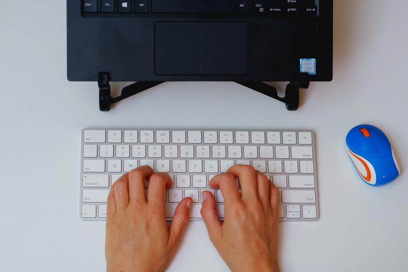 A woman's hands typing on a keyboard next to a mouse.