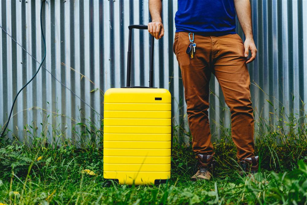 A man standing next to a yellow suitcase.