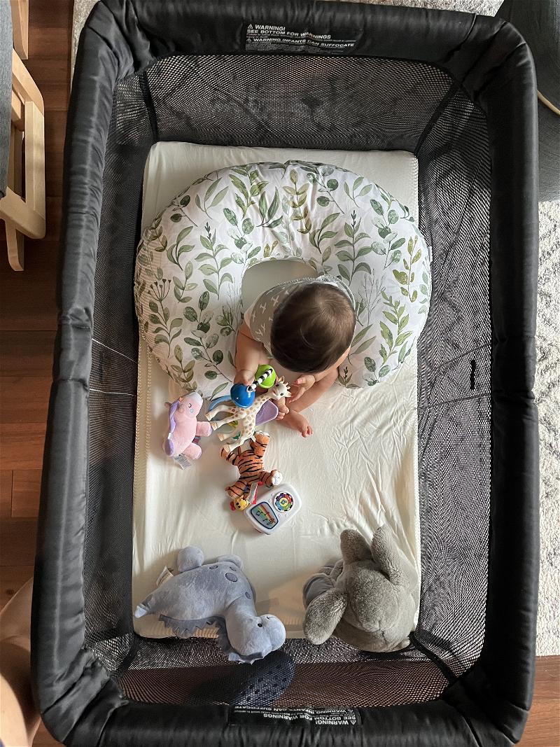 An infant in the Baby Bjorn travel crib playing with toys