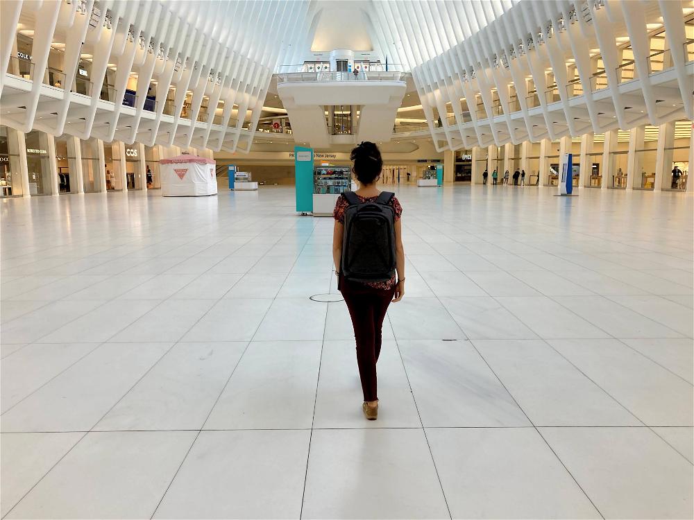 Woman wearing the gray Small Expandable Knack Pack while walking through the empty Oculus shopping mall at the world trade center transit hub
