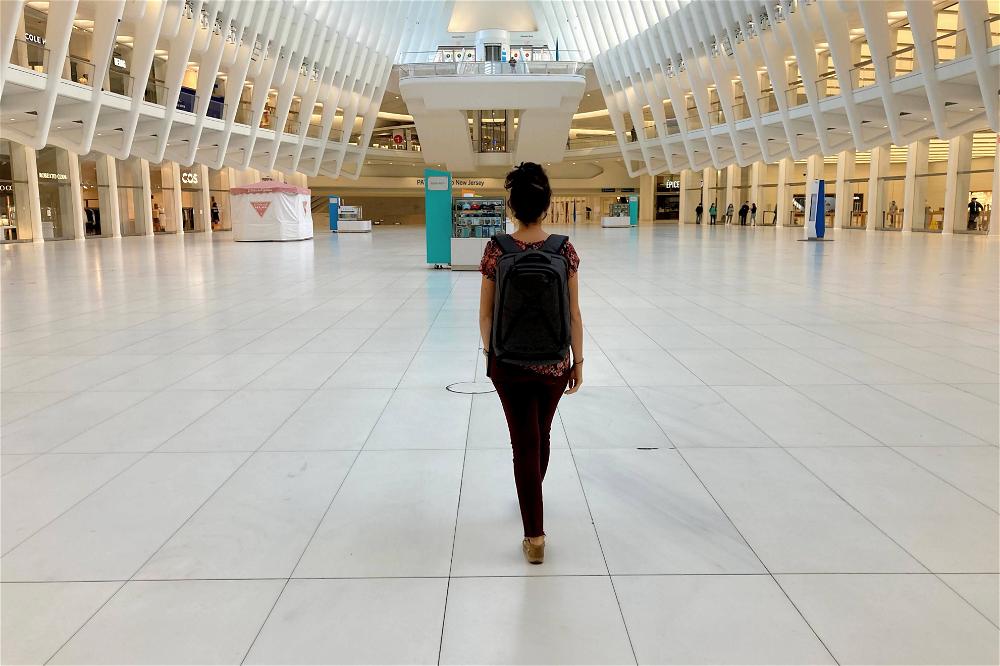 Woman wearing the gray Small Expandable Knack Pack while walking through the empty Oculus shopping mall at the world trade center transit hub