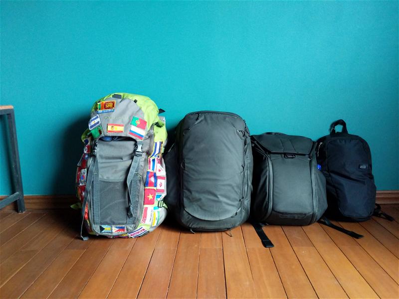 4 travel backpacks in a room with a blue wall.