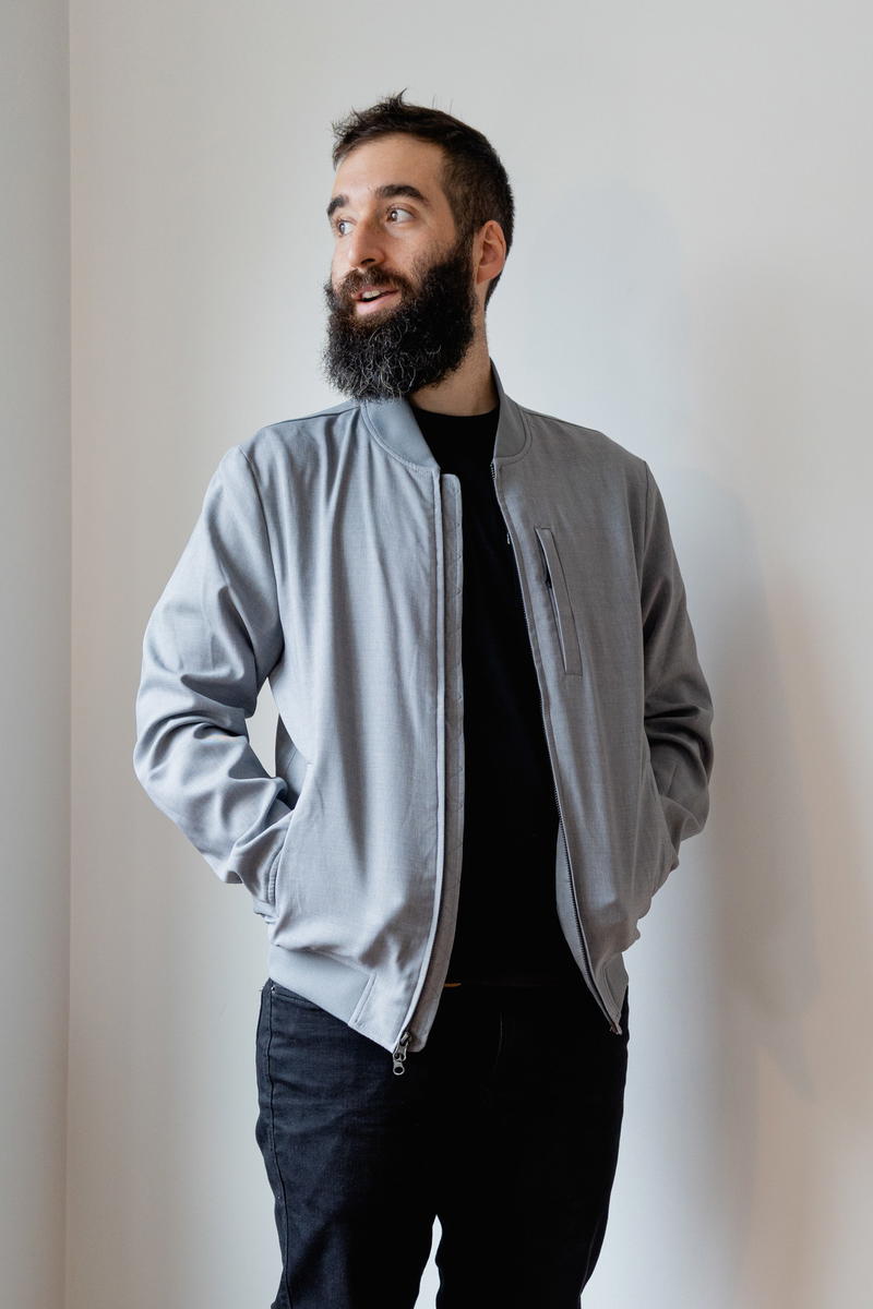 A bearded man wearing a grey bomber jacket.