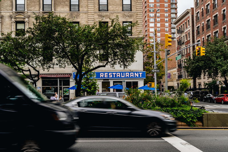 Cars driving by Broadway on the upper west side near the seinfeld restaurant