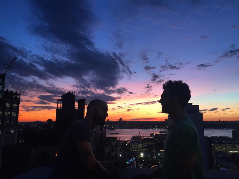 Two men standing on top of a building at sunset.