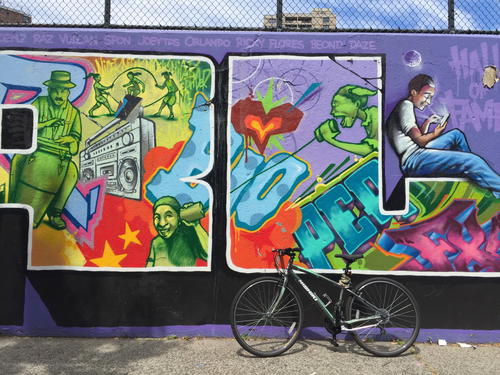 A bike is parked in front of a colorful graffiti wall.