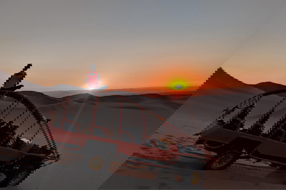 A person sitting on top of a jeep in the desert.