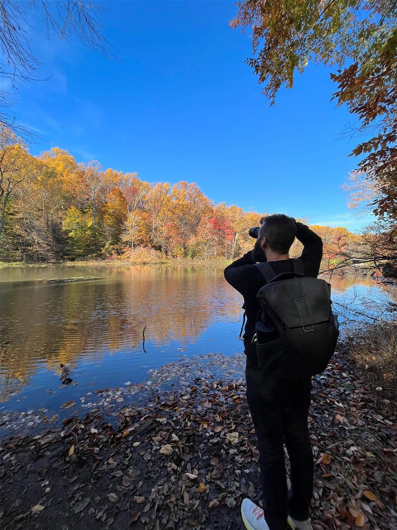 A man with a backpack is taking pictures of a lake.