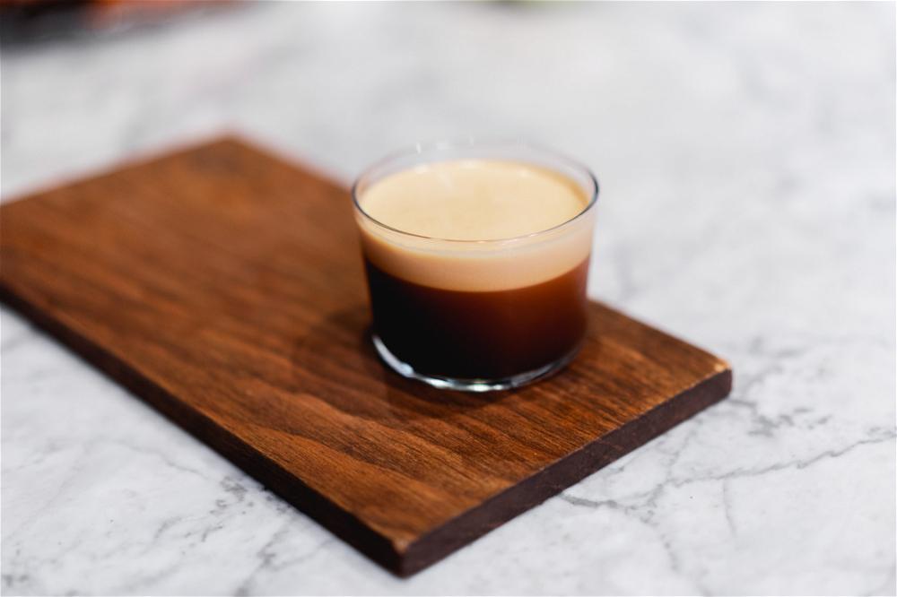 A glass of espresso on a wooden cutting board.