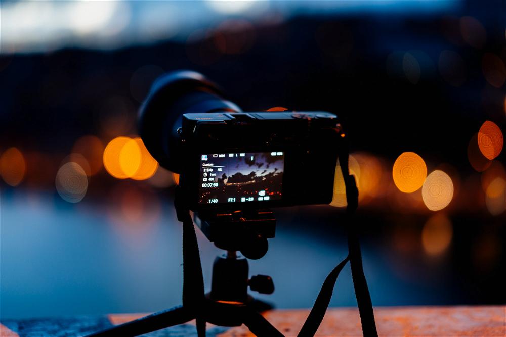 A camera sits on a tripod in front of a city at night.