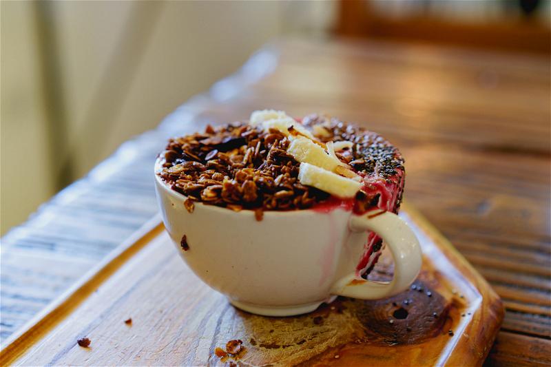 A cup of granola on a wooden tray.