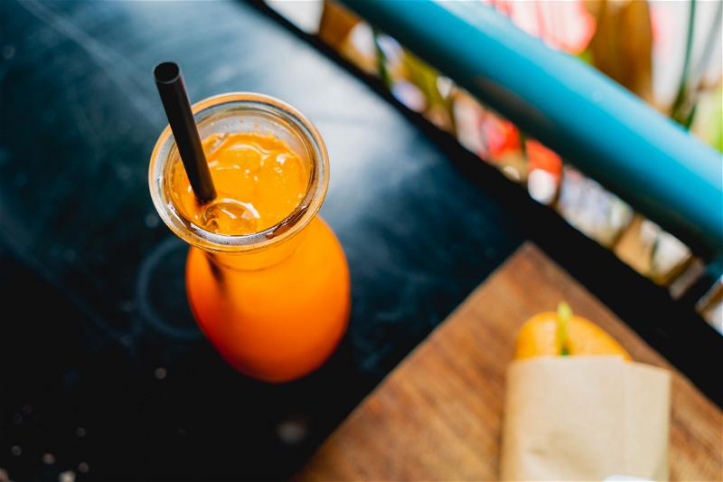 A glass of orange juice with a straw sitting on a table.