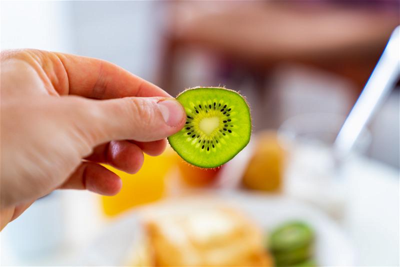 A person is holding a slice of kiwi fruit.
