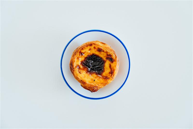 Pastel de nata on a white plate with blue border on a white table