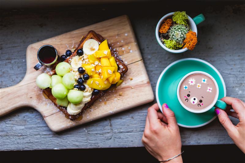 A wooden cutting board with fruit and a cup of coffee.