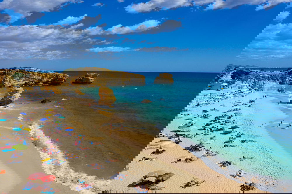 Turquoise and blue waters at a sandy beach with rock formations in Portugal