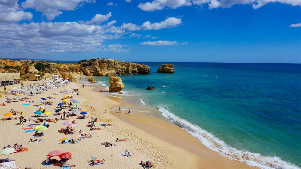Turquoise and blue waters at a sandy beach with rock formations in Portugal